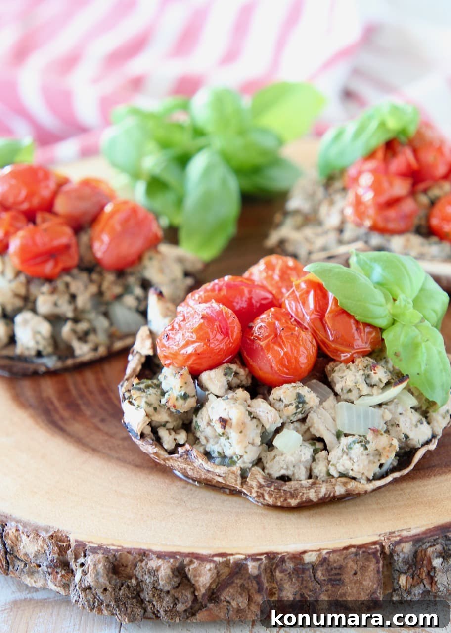Whole30 Italian Stuffed Portobello Mushrooms Recipe 2 Stuffed portobello mushrooms filled with ground turkey, cherry tomatoes and fresh basil leaves sitting on round wood cutting board with red and white striped towel in background