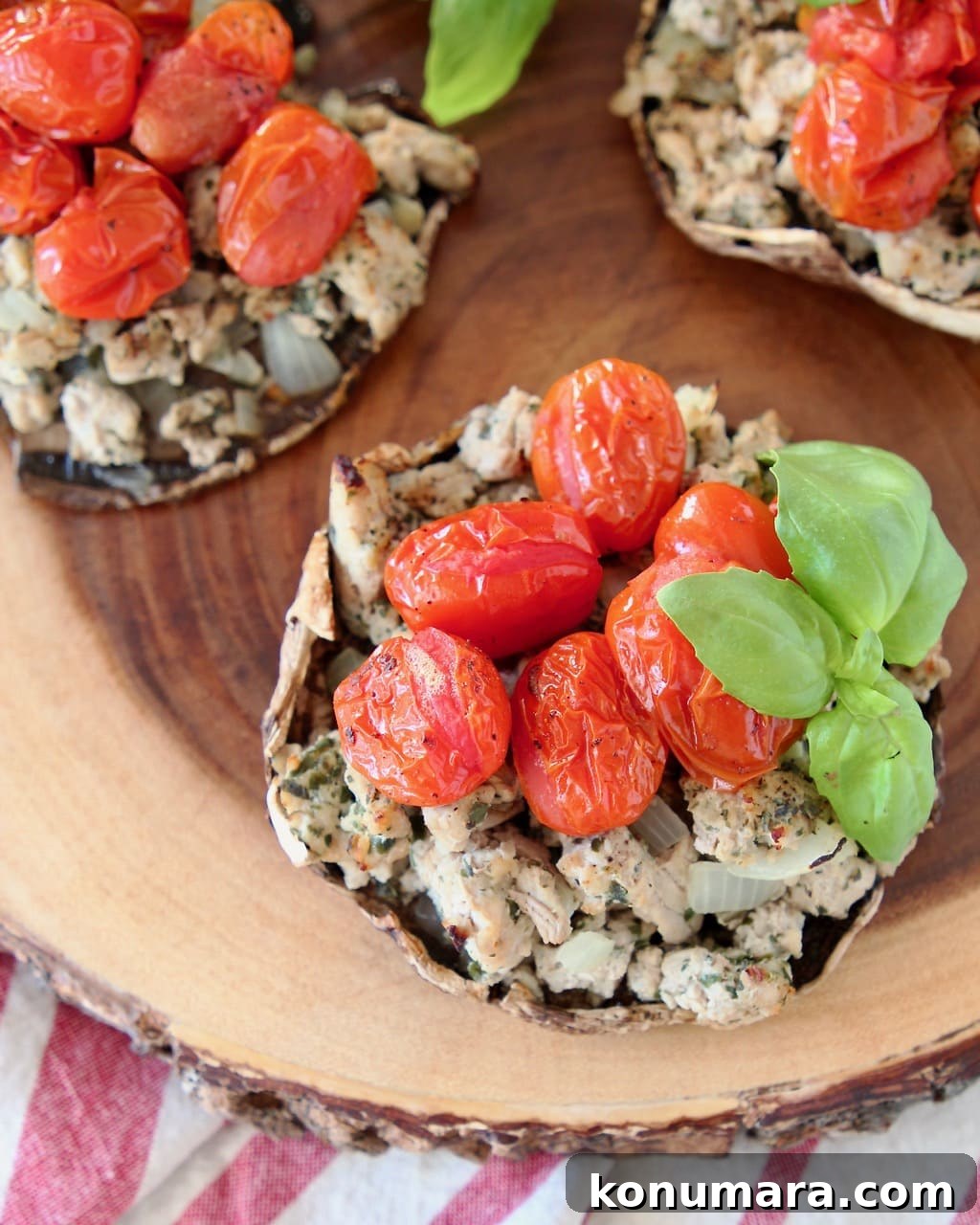 Whole30 Italian Stuffed Portobello Mushrooms Recipe 3 Overhead shot of stuffed portobello mushrooms filled with ground turkey, cherry tomatoes and fresh basil leaves, sitting on a round, raw edge wood cutting board, sitting on a red and white striped towel
