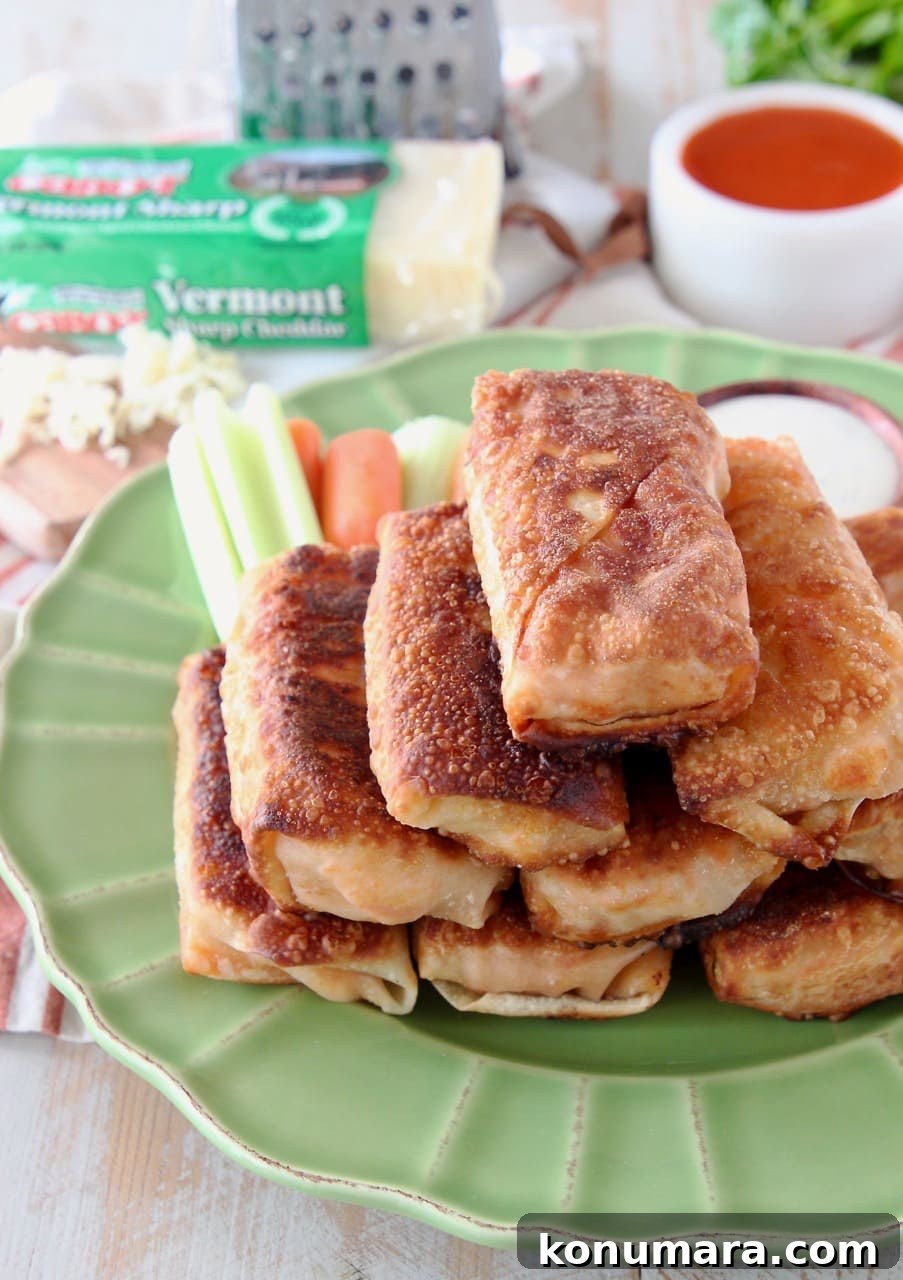 Crispy Buffalo Chicken Egg Rolls Recipe with Blue Cheese Dip 3 Buffalo chicken egg rolls piled up on top of green plate with carrot sticks and celery sticks in the background