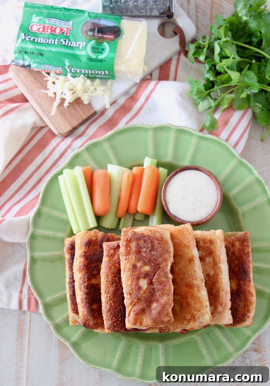 Crispy Buffalo Chicken Egg Rolls Recipe with Blue Cheese Dip 5 Overhead shot of buffalo chicken egg rolls stacked on top of each other on a green plate with carrot and celery sticks and a wood ramekin of ranch dressing
