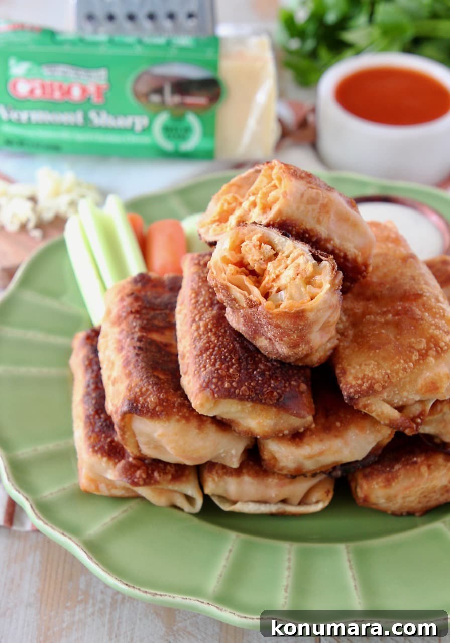 Crispy Buffalo Chicken Egg Rolls Recipe with Blue Cheese Dip 6 Buffalo chicken egg rolls stacked on each other on a green plate with the top egg roll cut in half
