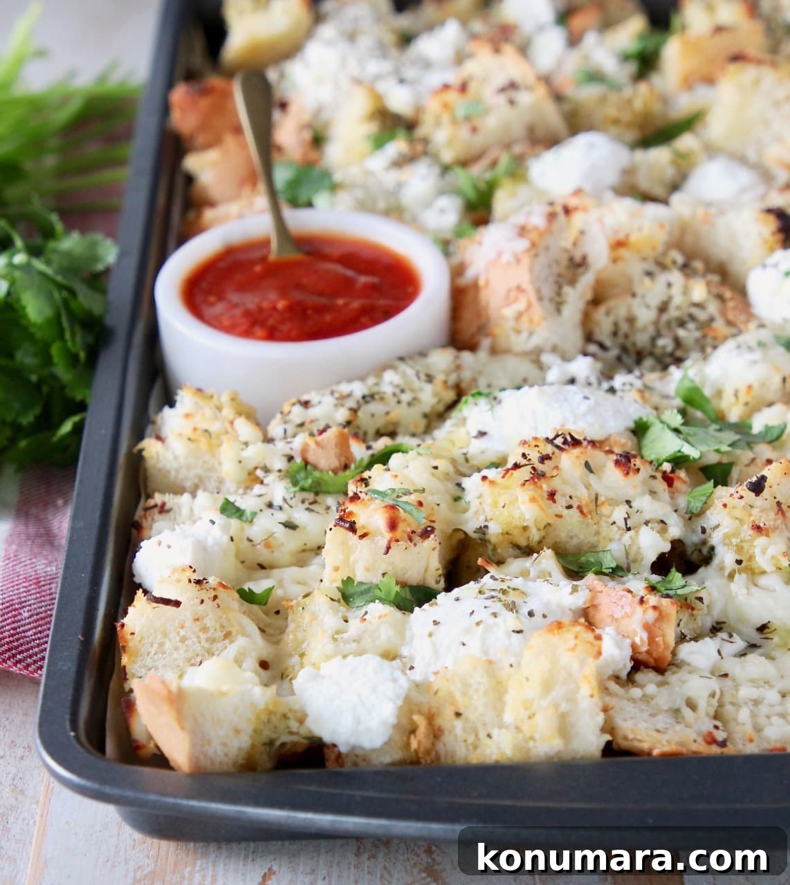 Cheesy Garlic Bread Nachos Recipe 2 Cubed garlic bread, covered in cheese and fresh parsley on a baking sheet with a small bowl of marinara sauce