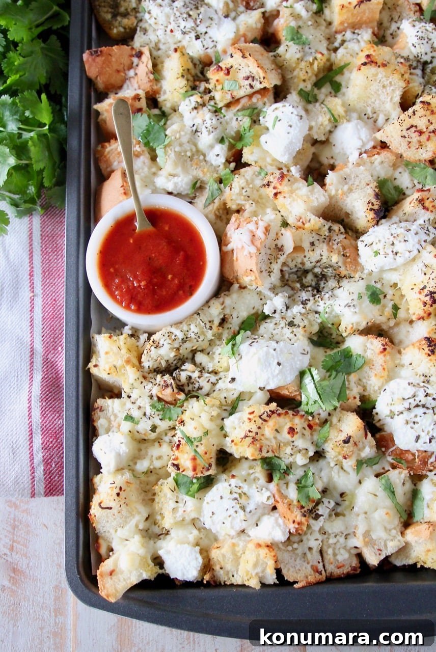 Cheesy Garlic Bread Nachos Recipe 6 Cheesy garlic bread nachos on a baking sheet with a small bowl of marinara sauce in the corner with a spoon in the bowl