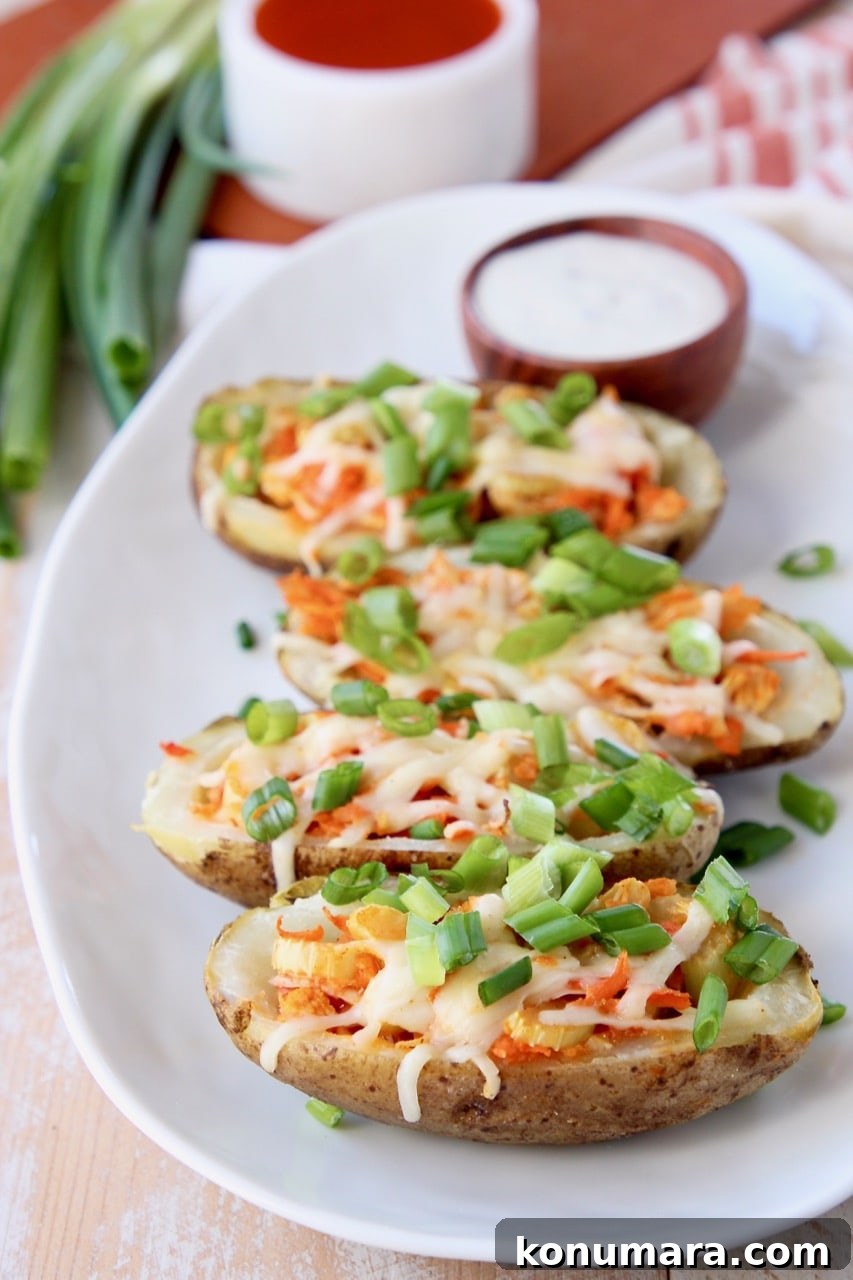 Crispy Buffalo Chicken Potato Skins 3 Buffalo chicken on potato skins, topped with diced green onions with a wood bowl of ranch dressing on the plate behind the potato skins