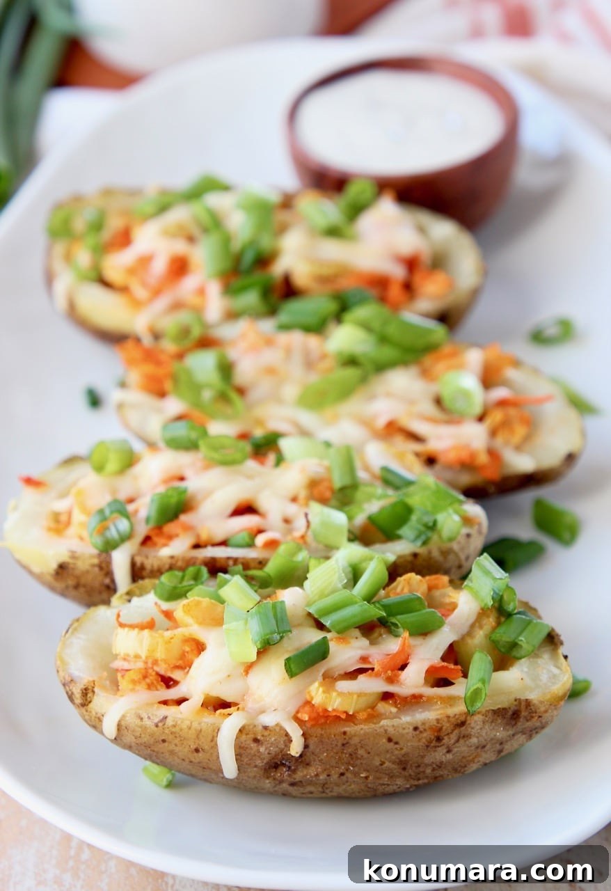 Crispy Buffalo Chicken Potato Skins 6 Buffalo Chicken Potato Skins topped with diced green onions on white plate with side ramekin of ranch dressing