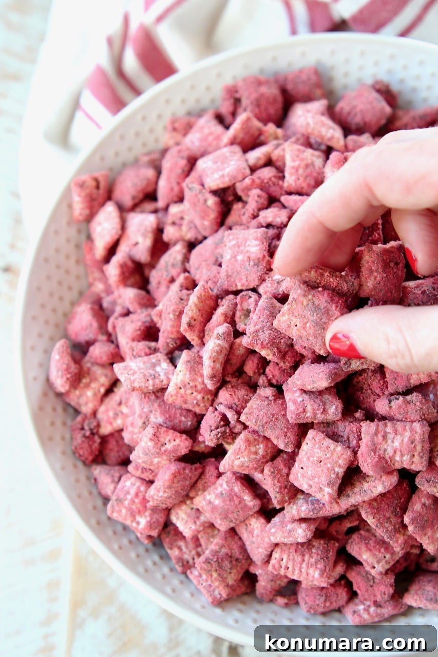 Hand reaching in grabbing red velvet puppy chow out of a white bowl