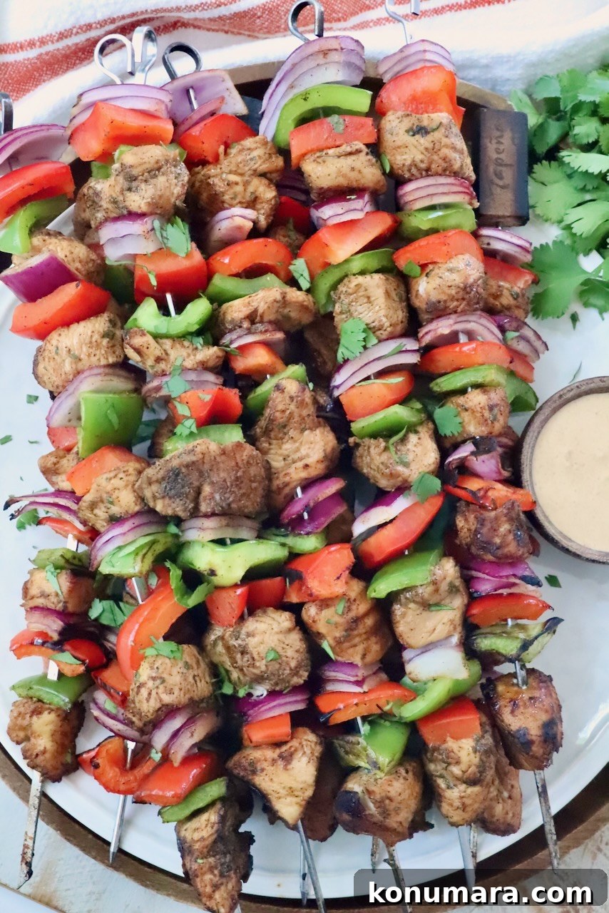 fajita chicken skewers stacked up on a plate with a small bowl of creamy sauce on the side next to fresh cilantro