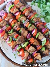 chicken fajita skewers stacked up on a white plate next to fresh cilantro leaves