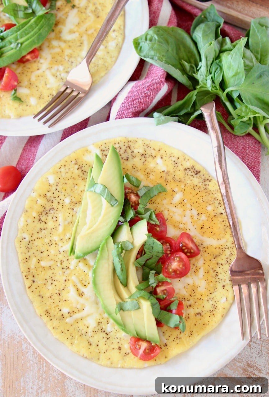 Omelette topped with sliced avocado, diced tomatoes and fresh basil on white plate with copper fork on the side of the plate