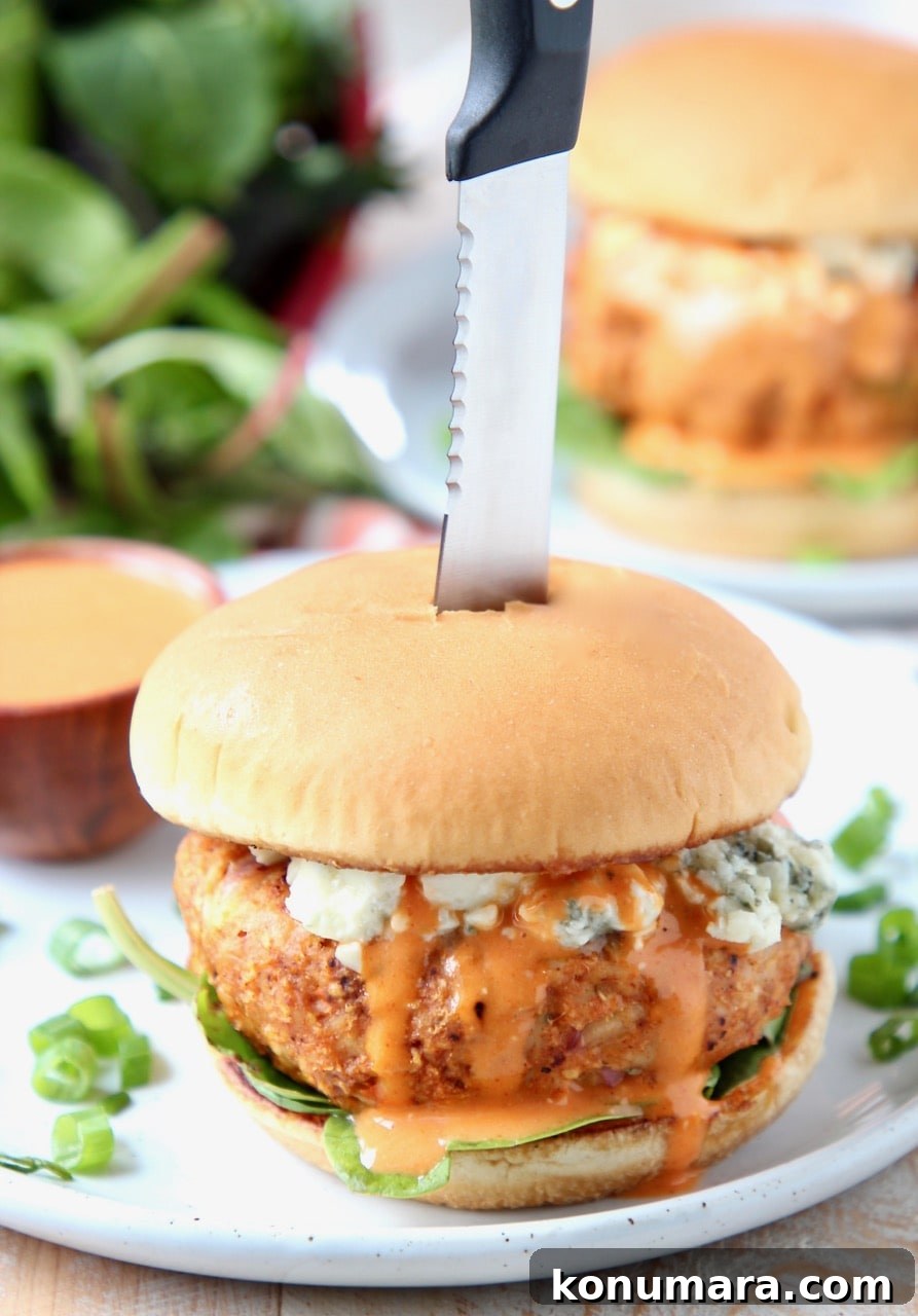 Spicy Buffalo Chicken Burgers with Blue Cheese Slaw 2 Buffalo chicken burger on plate, topped with blue cheese crumbles with knife in the middle of the burger