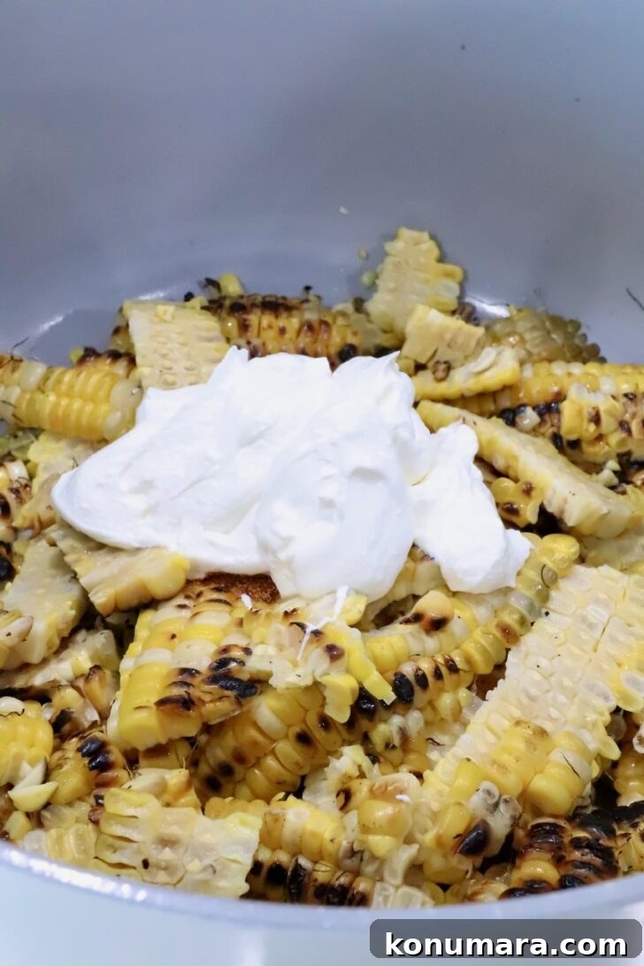 grilled corn kernels with char marks topped with sour cream in a white pot