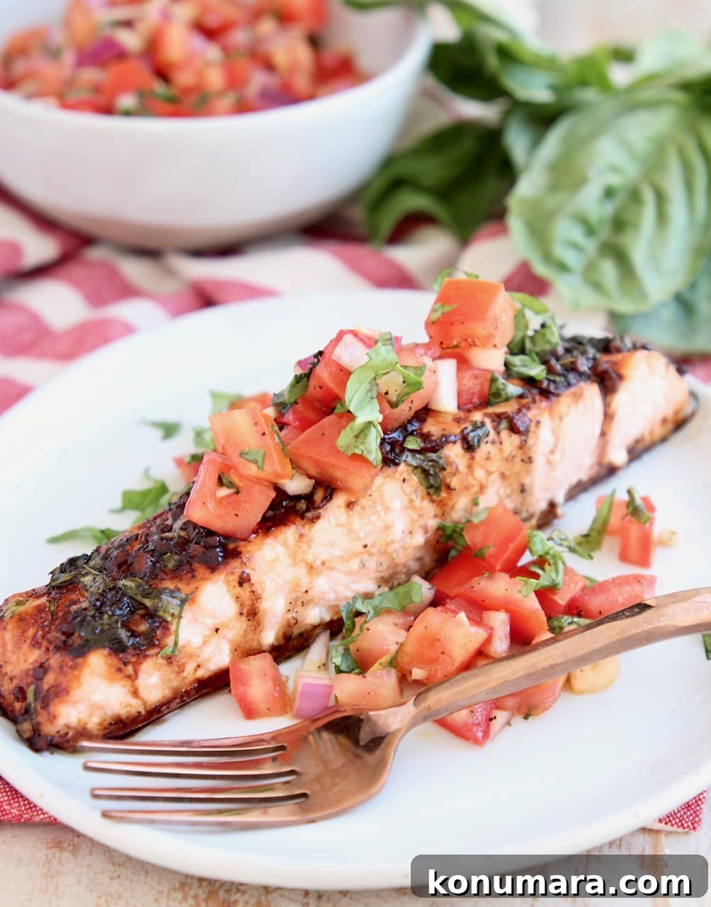 Grilled Salmon with Tomato Bruschetta 2 A piece of baked salmon on a white plate topped with tomato basil bruschetta with a copper fork on the side of the plate
