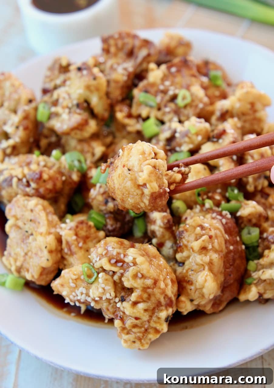 Crispy Korean-Style Fried Cauliflower with Gochujang Glaze 2 Korean fried cauliflower on plate with chopsticks picking up one piece of cauliflower