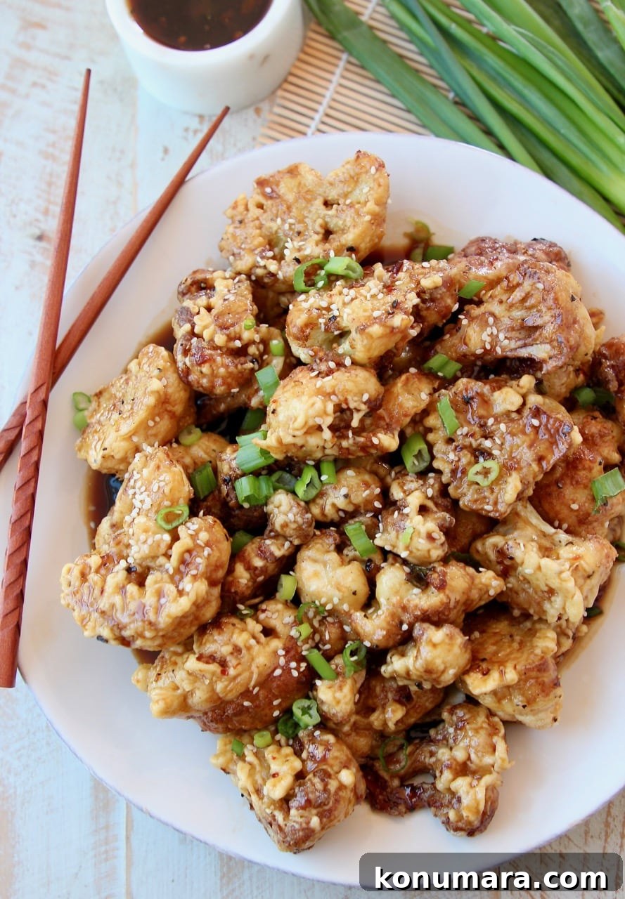 Crispy Korean-Style Fried Cauliflower with Gochujang Glaze 3 Fried cauliflower piled up on white plate topped with Korean BBQ Sauce and diced green onions