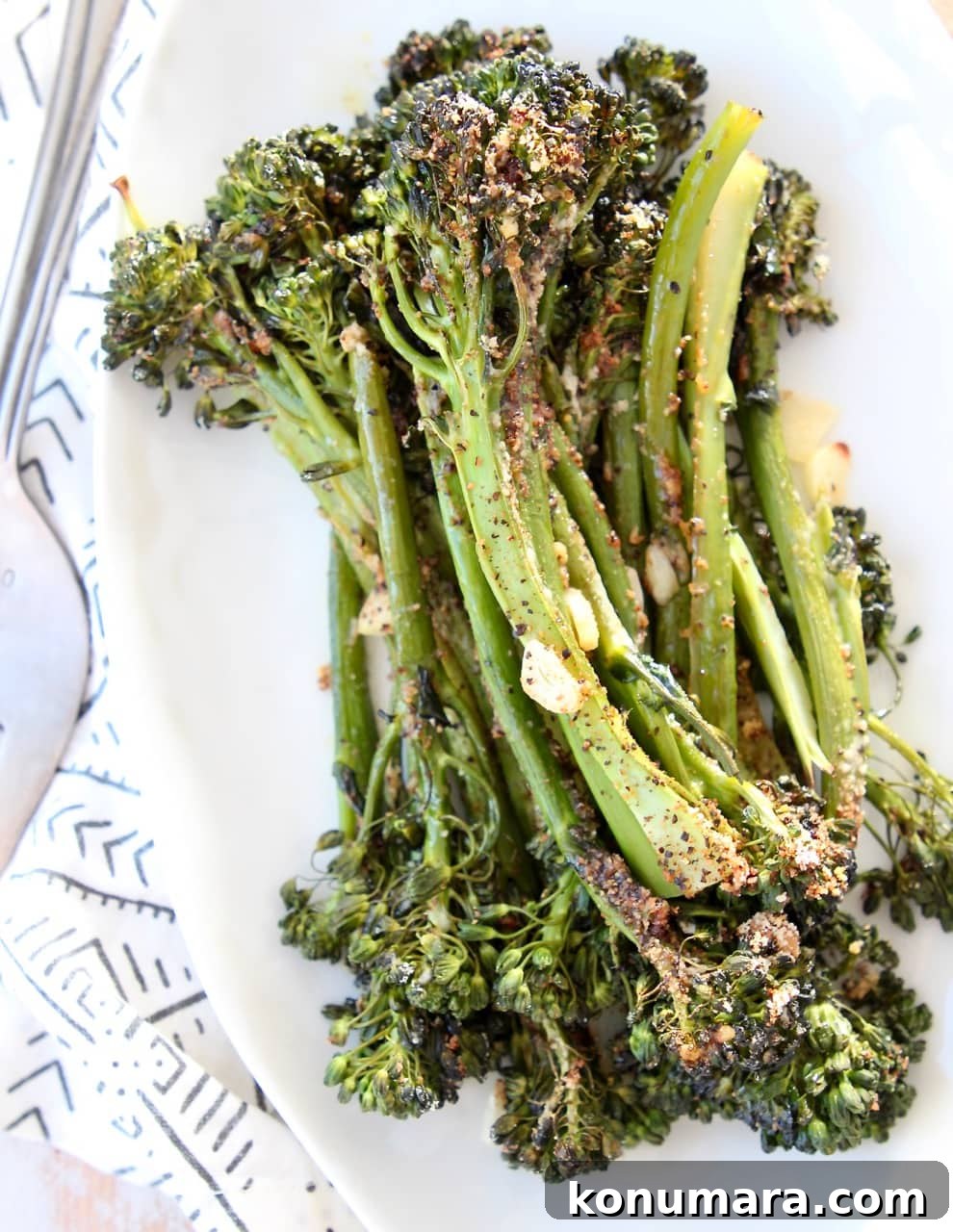 Garlic parmesan broccolini stacked up on top of each other on white plate