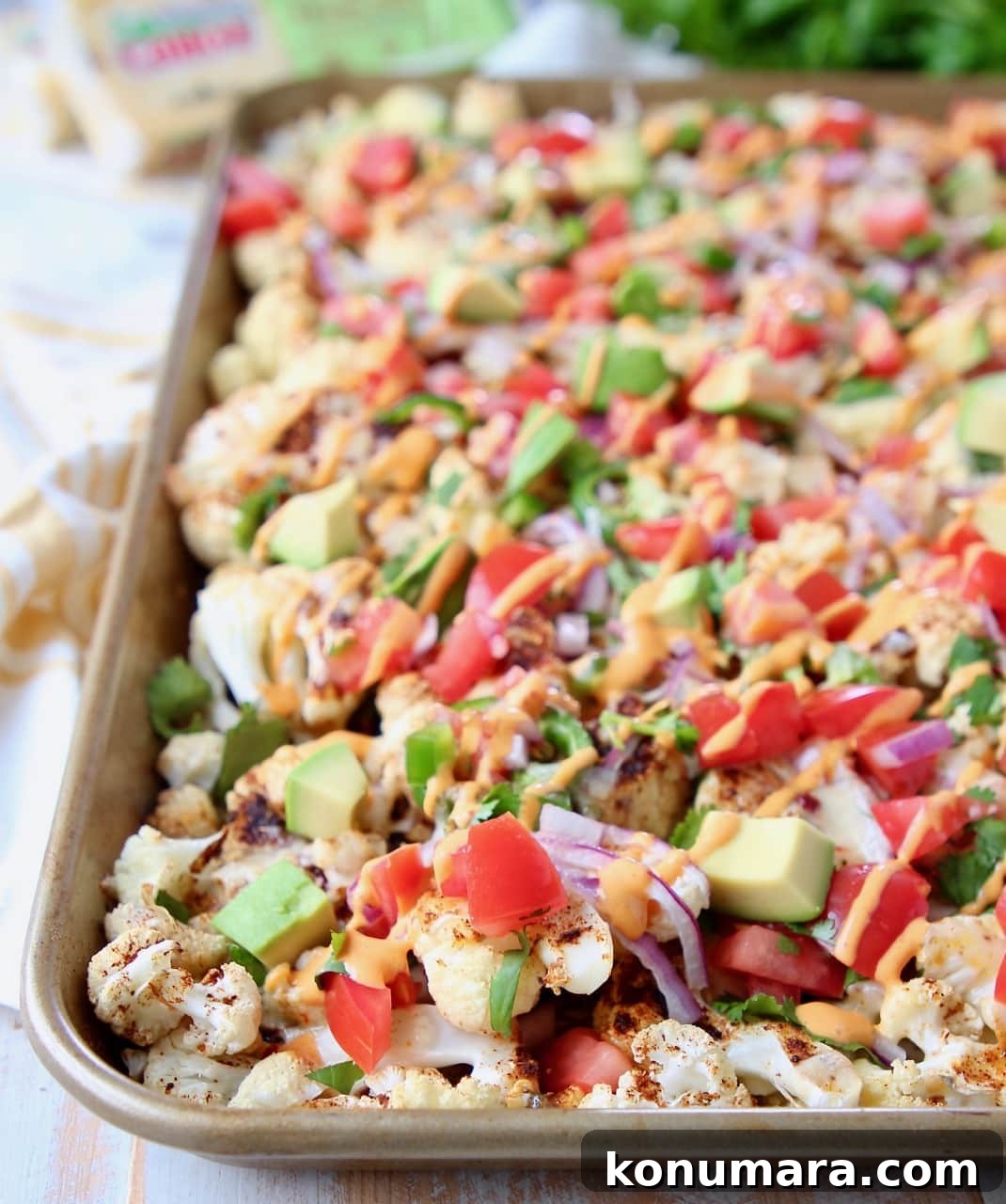 Cauliflower nachos on baking sheet topped with diced tomatoes and avocado