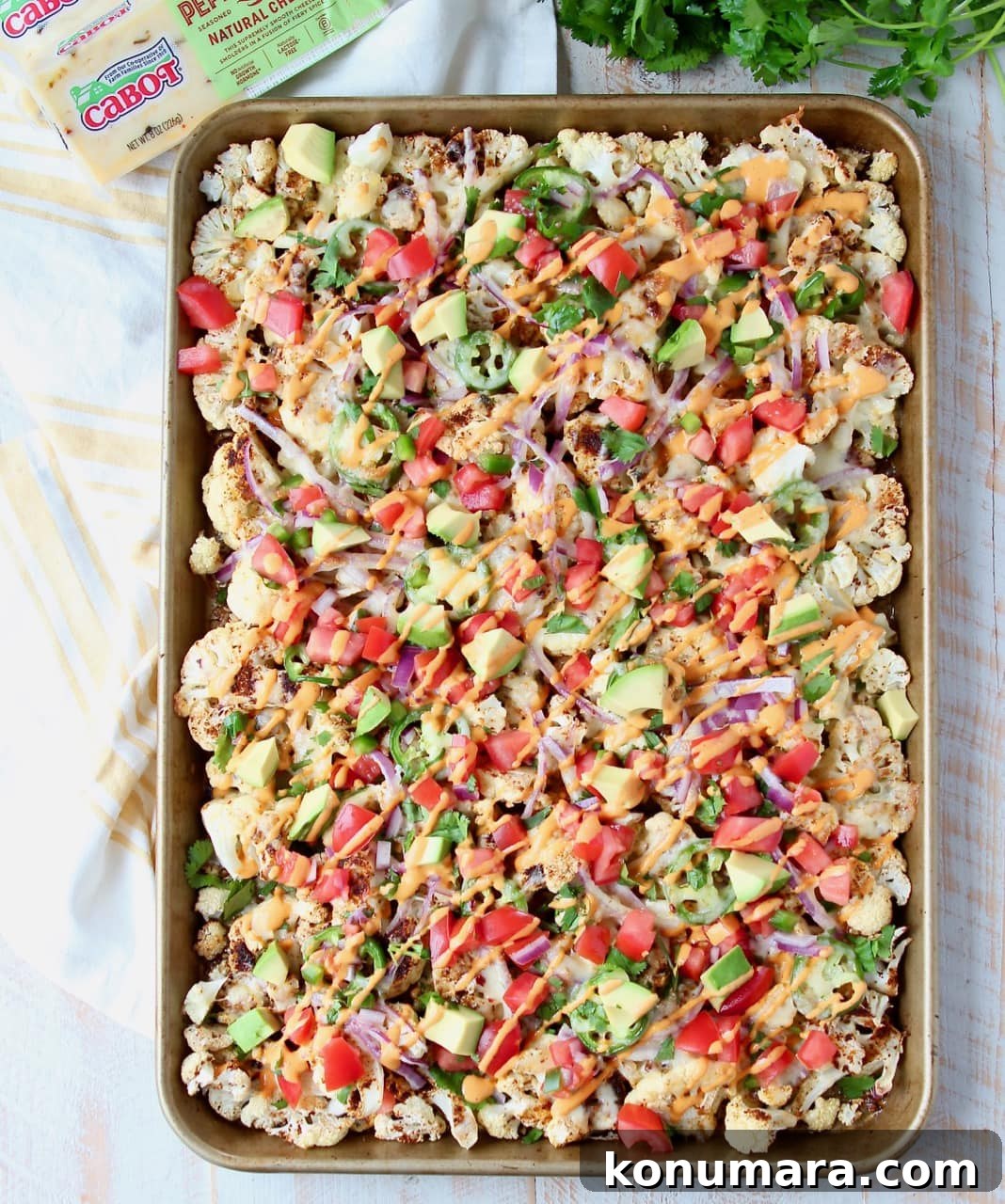 Overhead shot of cauliflower nachos on sheet pan with fresh cilantro and sliced jalapenos