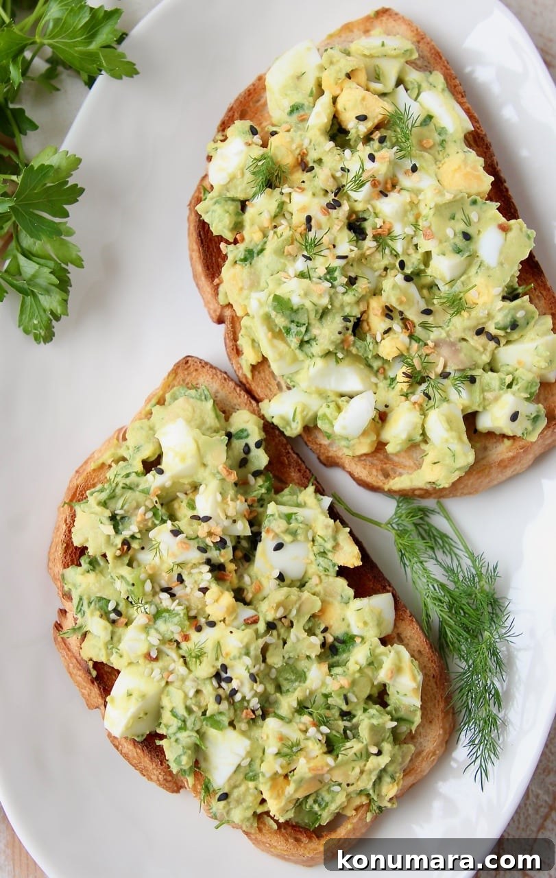 Avocado egg salad on two pieces of toast on a white plate with fresh dill