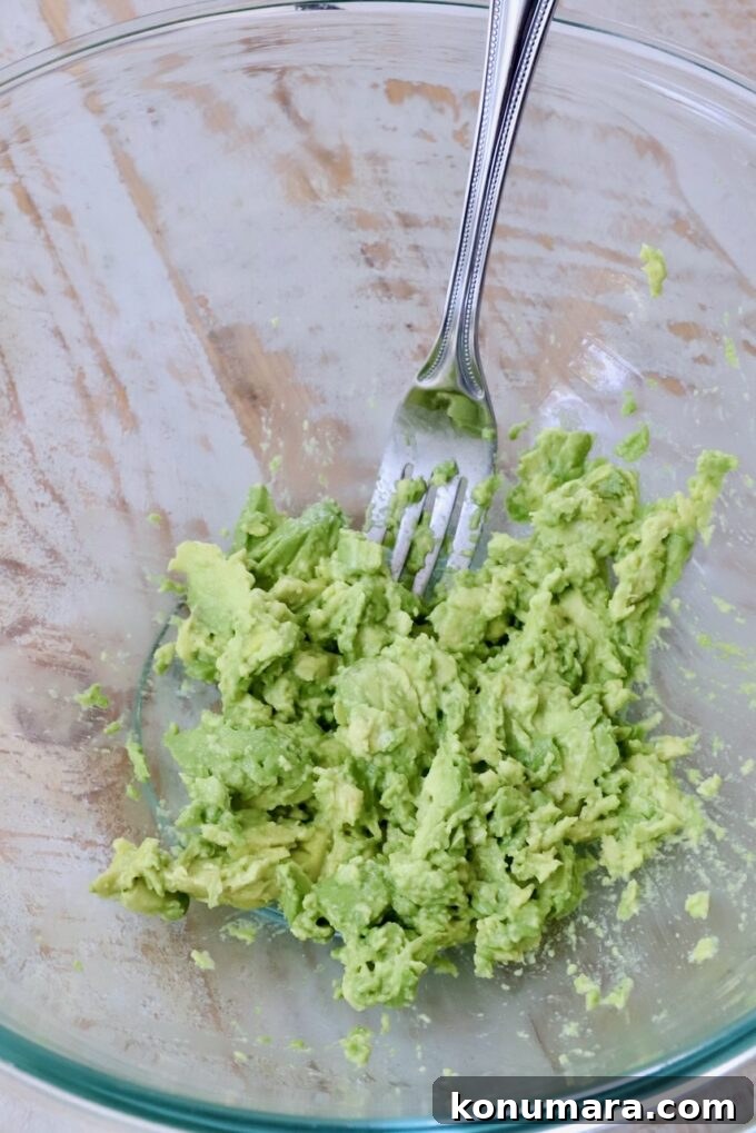 smashed avocado in a glass bowl with a fork