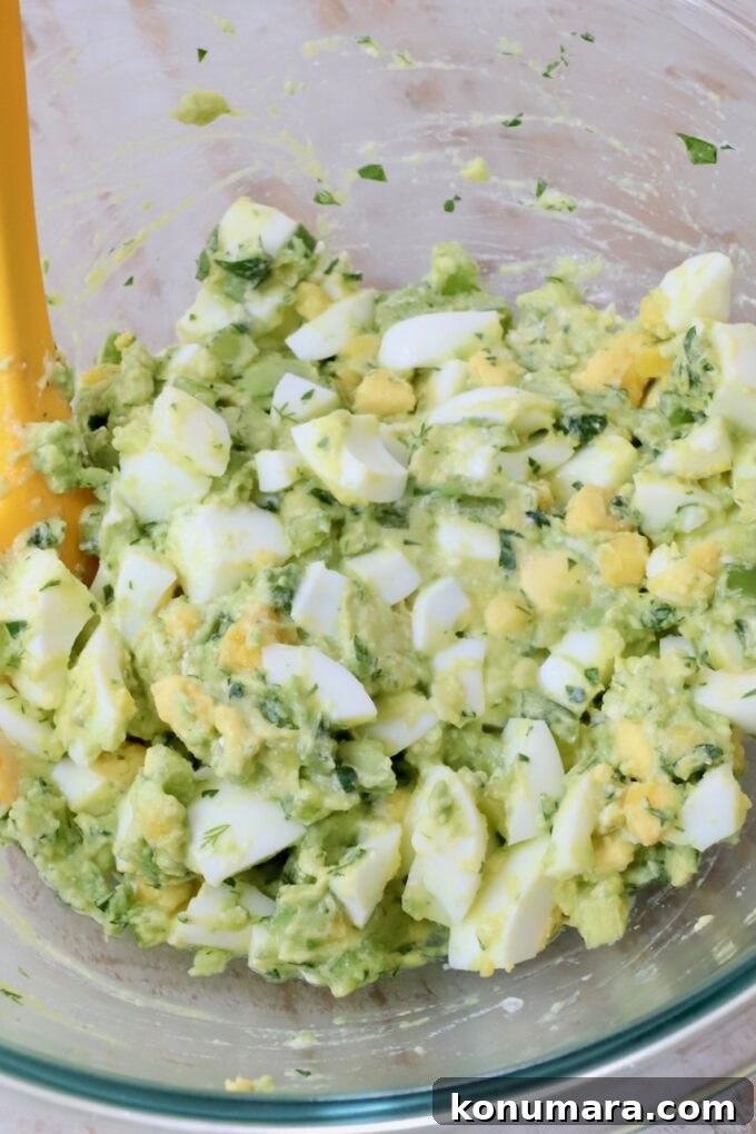 avocado egg salad in a glass bowl with a yellow spatula