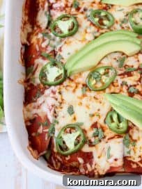 Overhead shot of enchiladas in casserole dish topped with sliced avocado and jalapenos