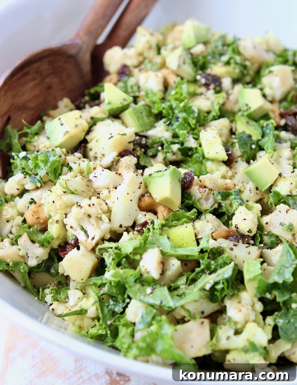 Roasted Cauliflower Salad with Lemon Tahini Dressing 2 Cauliflower salad with kale, raisins and avocado in white bowl with brown wooden spoon