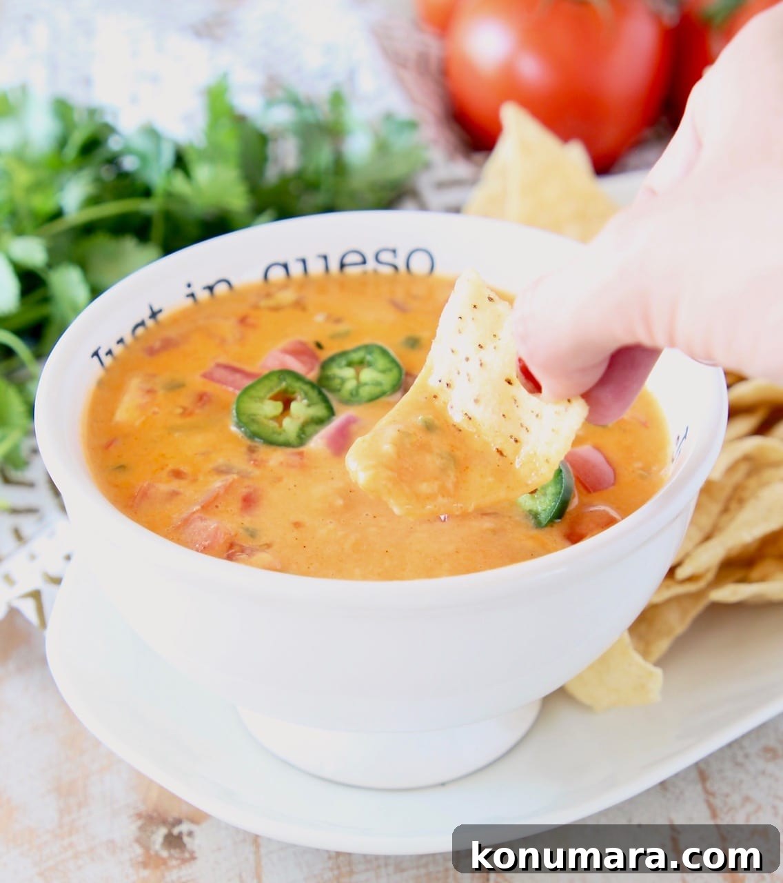 Hand dipping tortilla chip into buffalo queso dip