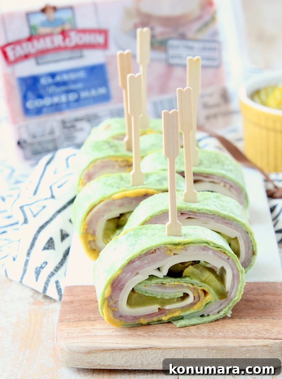 Pinwheel sandwich with ham, cheese, pickles and mustard, with toothpick in each piece, on a cutting board