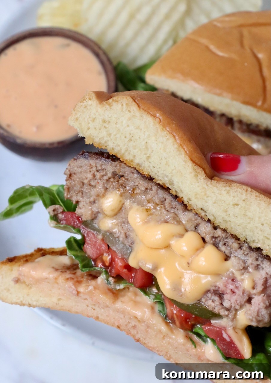 hand holding a burger stuffed with melted cheese over plate with chips