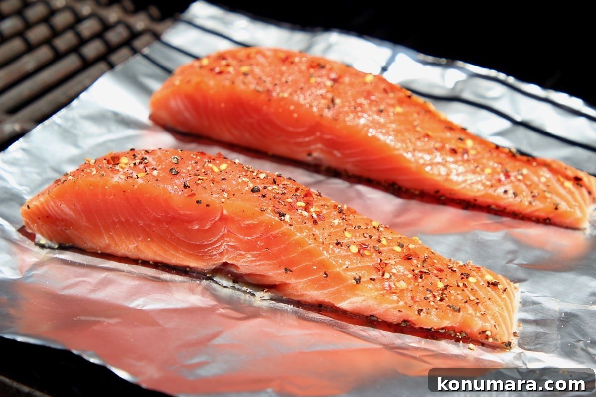 Two pieces of seasoned raw salmon on a piece of foil on the grill