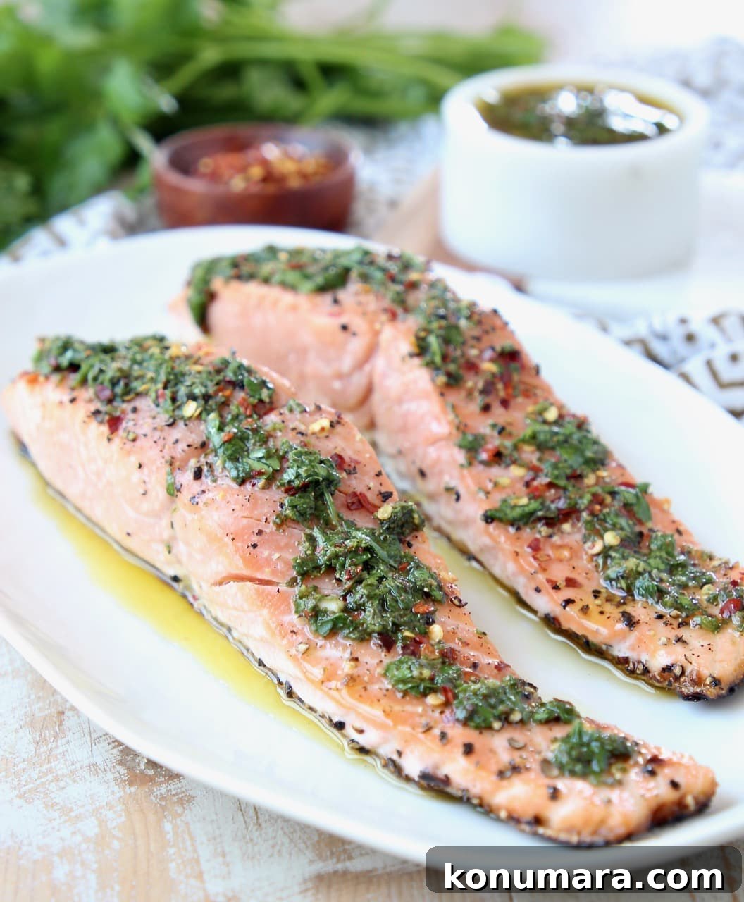 Two filets of grilled salmon on a white plate topped with chimichurri sauce