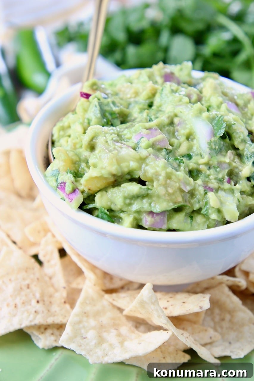 Tomatillo guacamole in white bowl, on plate with tortilla chips