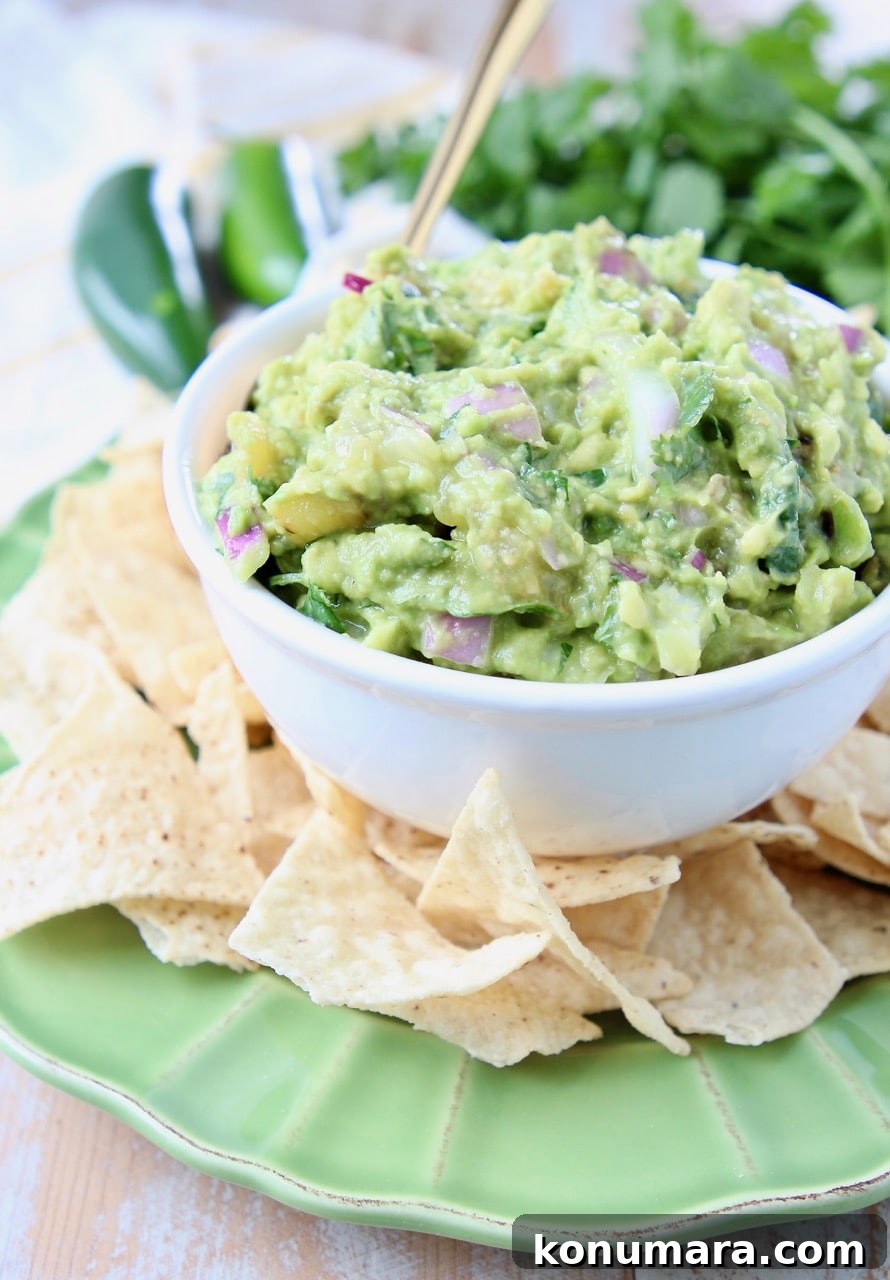 Tomatillo guacamole in white bowl on green plate, surrounded by tortilla chips