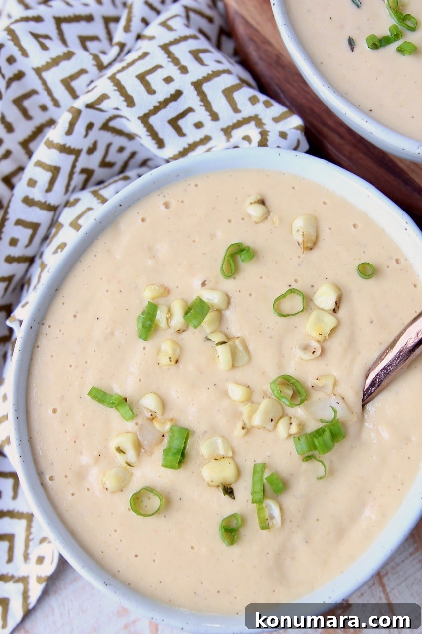 Creamy corn soup in bowl with corn kernels and green onions on top