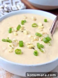 Corn soup in bowl topped with corn kernels and diced green onions