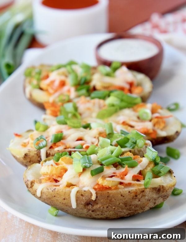 Slow Cooker Buffalo Chicken Recipe 10 Buffalo chicken potato skins lined up on a white oval plate topped with diced green onions with a small bowl of ranch dressing in the background