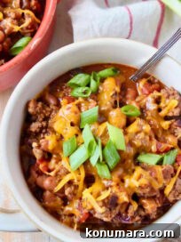 chili in a bowl topped with melted shredded cheese and diced green onions