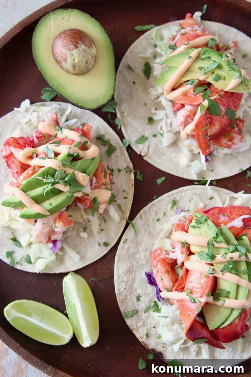 Overhead image of lobster tacos on wood tray with lime wedges and half an avocado