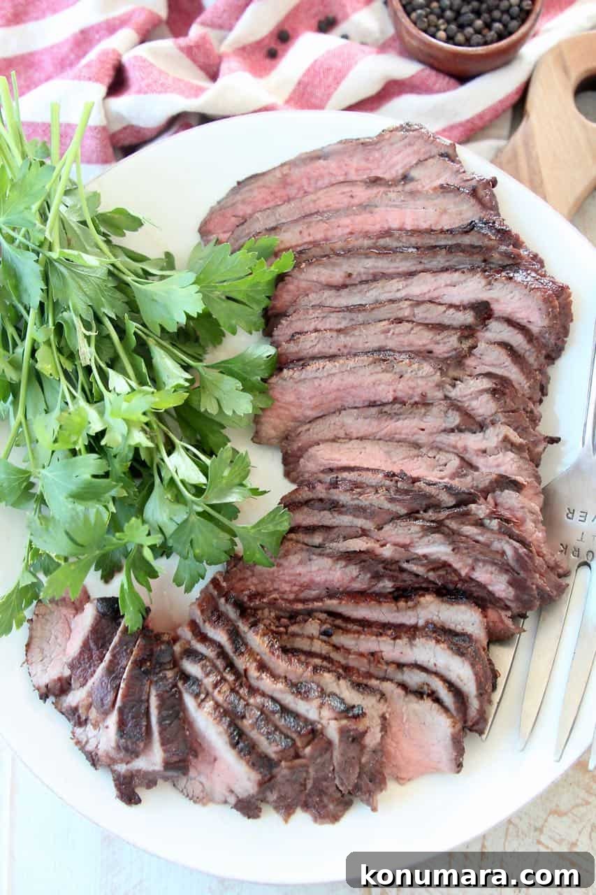 Sliced tri tip steak on white plate with fresh parsley