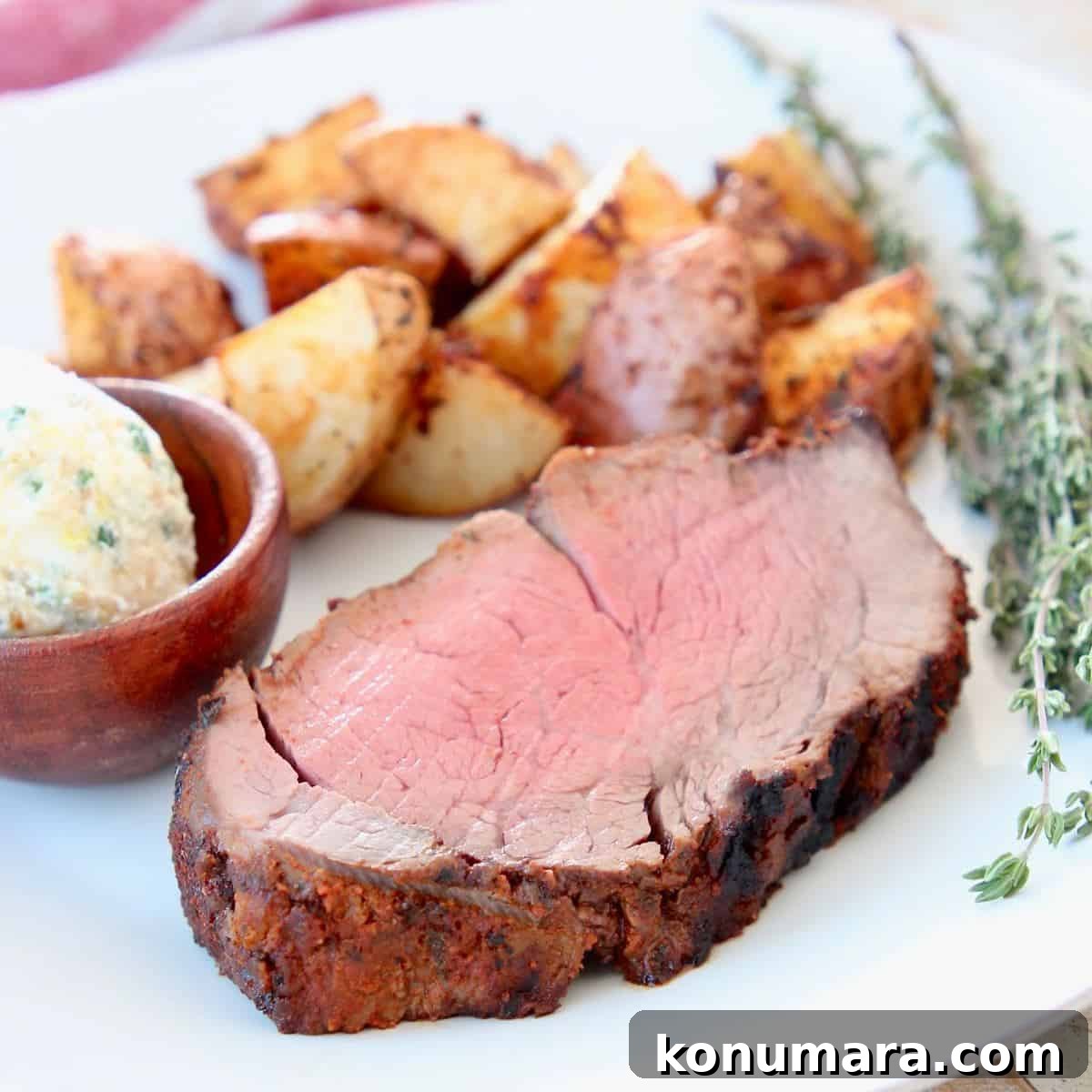 Slice of blackened beef tenderloin on plate with potatoes and herb butter in wood ramekin