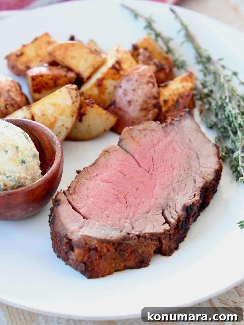 Thick sliced beef tenderloin on plate with herbs, potatoes and butter