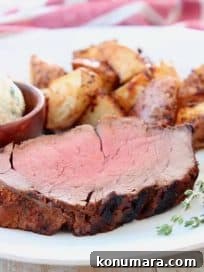 Slice of beef tenderloin on plate with fresh herbs and potatoes