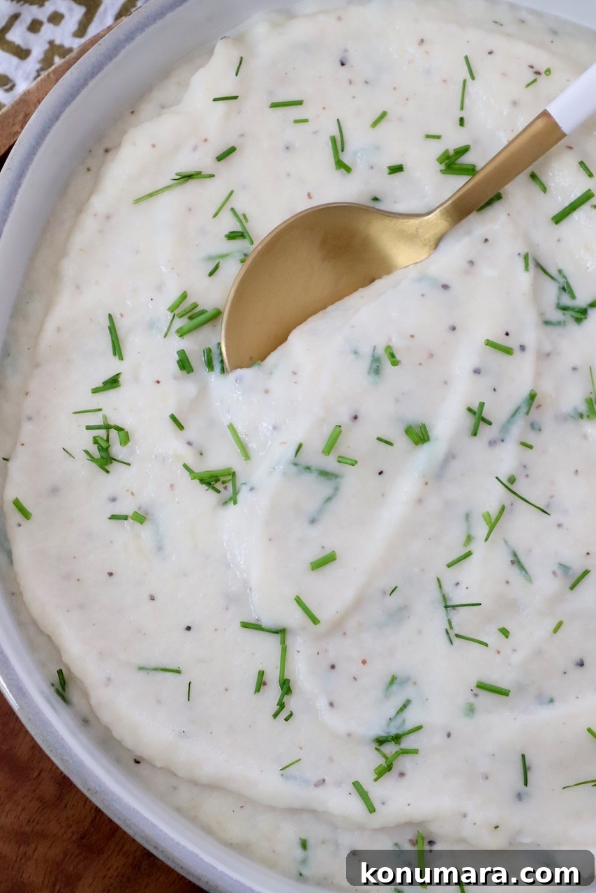 mashed cauliflower in a bowl with chopped chives and a serving spoon