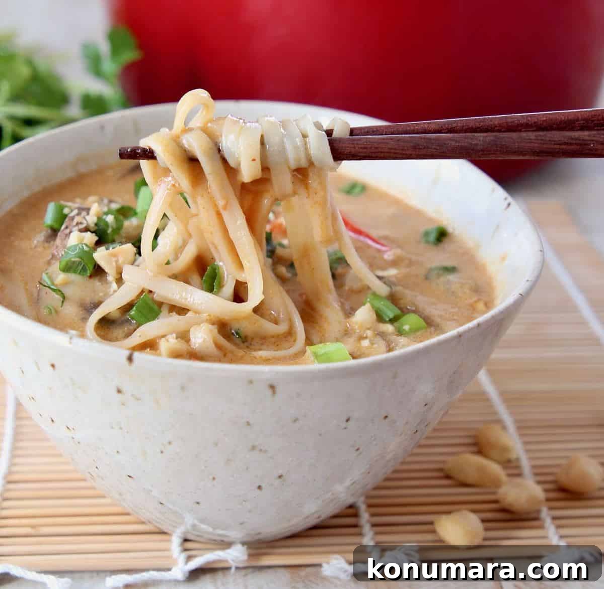 Creamy One-Pot Thai Peanut Noodle Soup 3 Chopsticks pulling noodles out of a bowl of soup