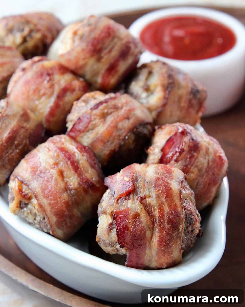 Bacon wrapped meatballs in white serving dish on wood serving tray
