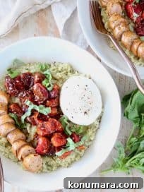 Bowl of pesto risotto topped with cherry tomatoes, sliced sausage and burrata cheese