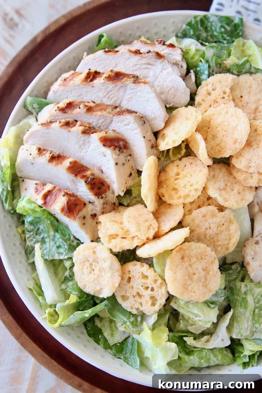 Bowl of caesar salad topped with sliced grilled chicken and parmesan cheese crisps