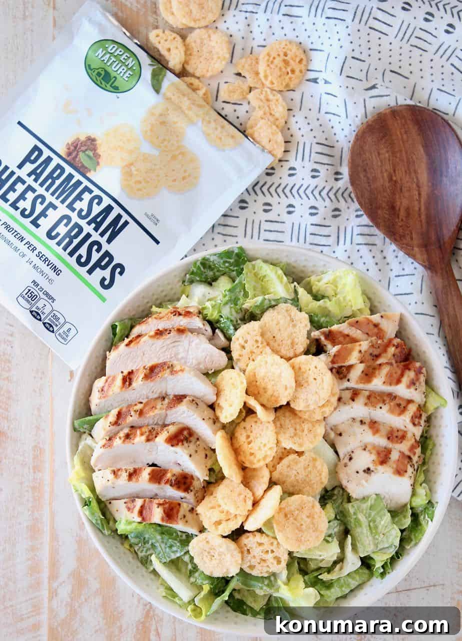 Salad in bowl topped with sliced grilled chicken and parmesan crisps