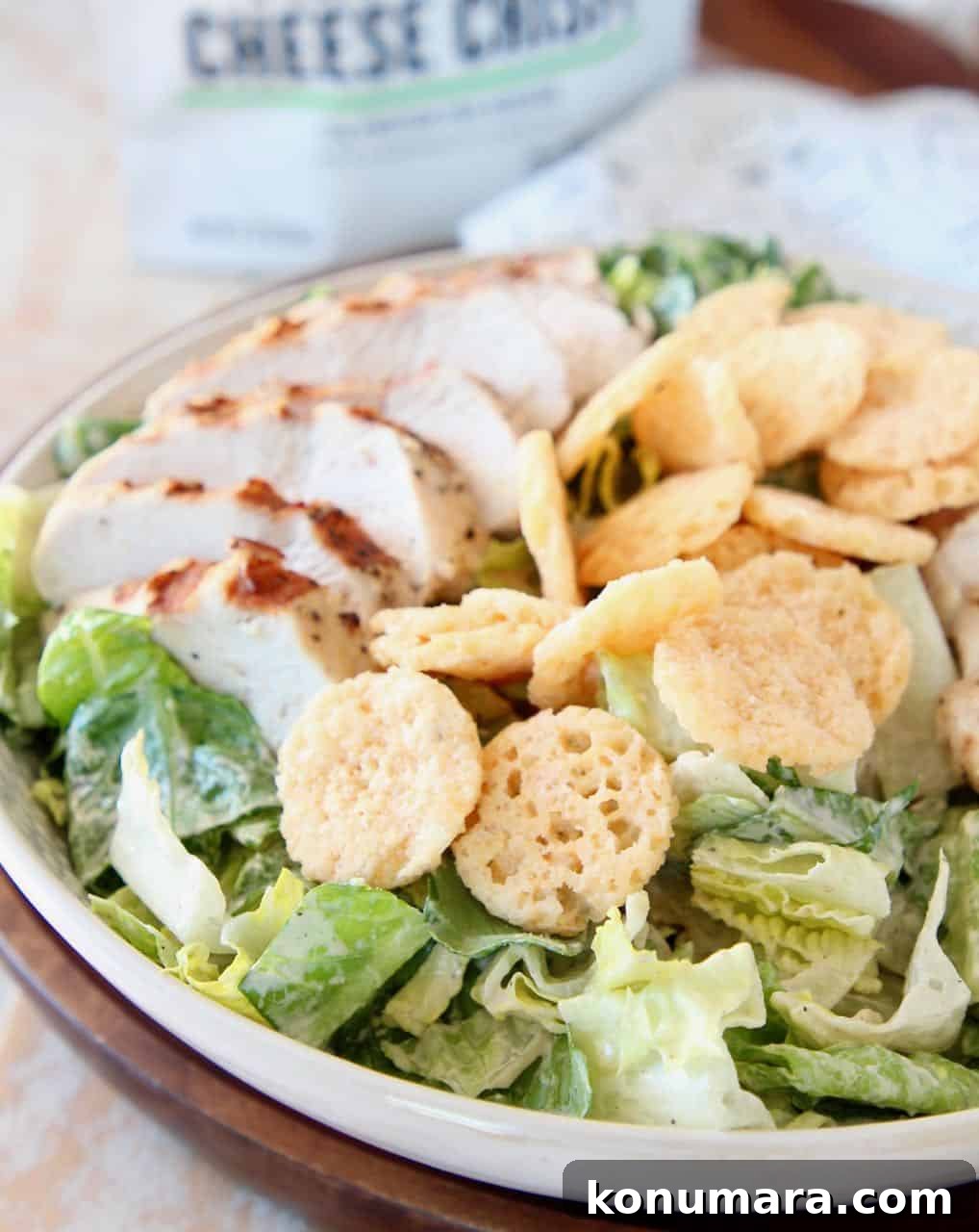 Chicken caesar salad in white bowl topped with parmesan cheese crisps