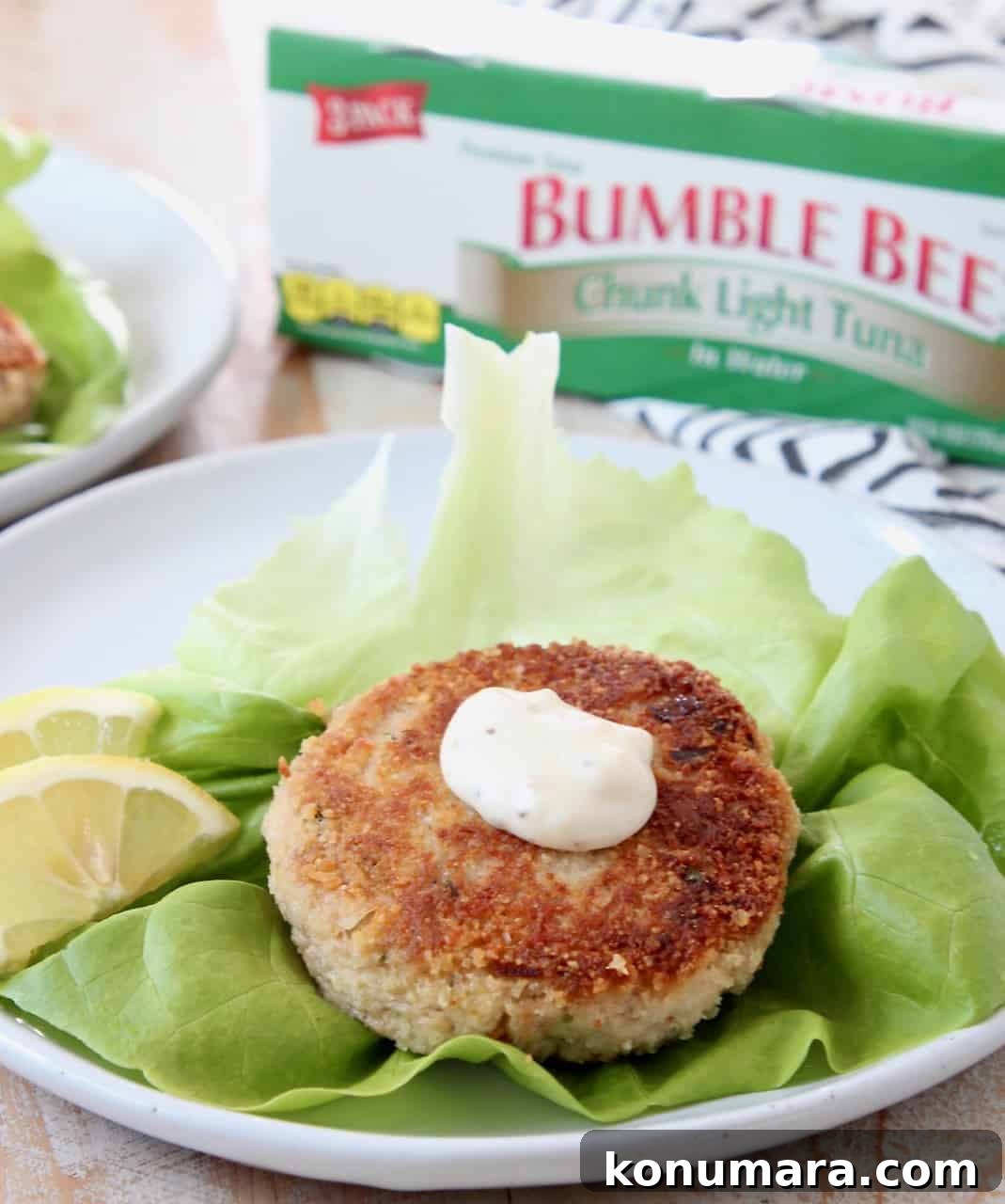 Tuna patty on leaf of lettuce with lemon wedges on plate